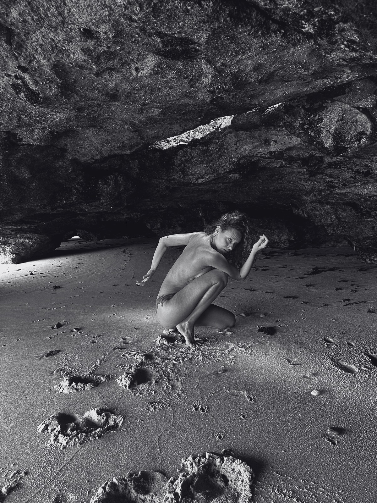 Mulher em contato com o próprio corpo no encontro entre areia e mar